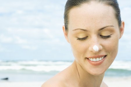mulher na praia usando protetor solar no nariz